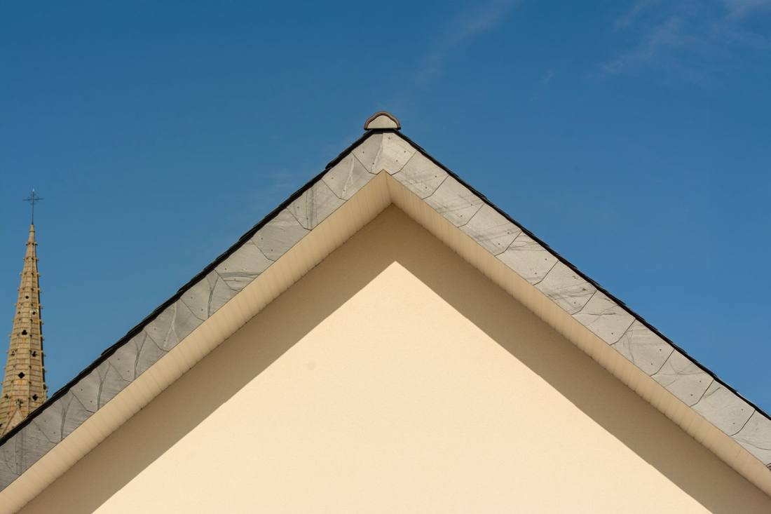 Minimalist architectural shot of building roof and church tower against clear sky.